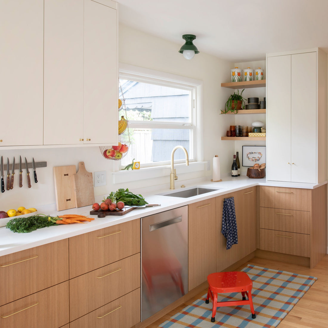 Bright remodeled kitchen with light wood lower cabinets, white counters, brass faucet, open wood shelves, hanging fruit basket