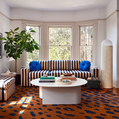 Striped navy and beige sofa with blue pillows in sunlit bay-window room with white coffee table and orange patterned rug