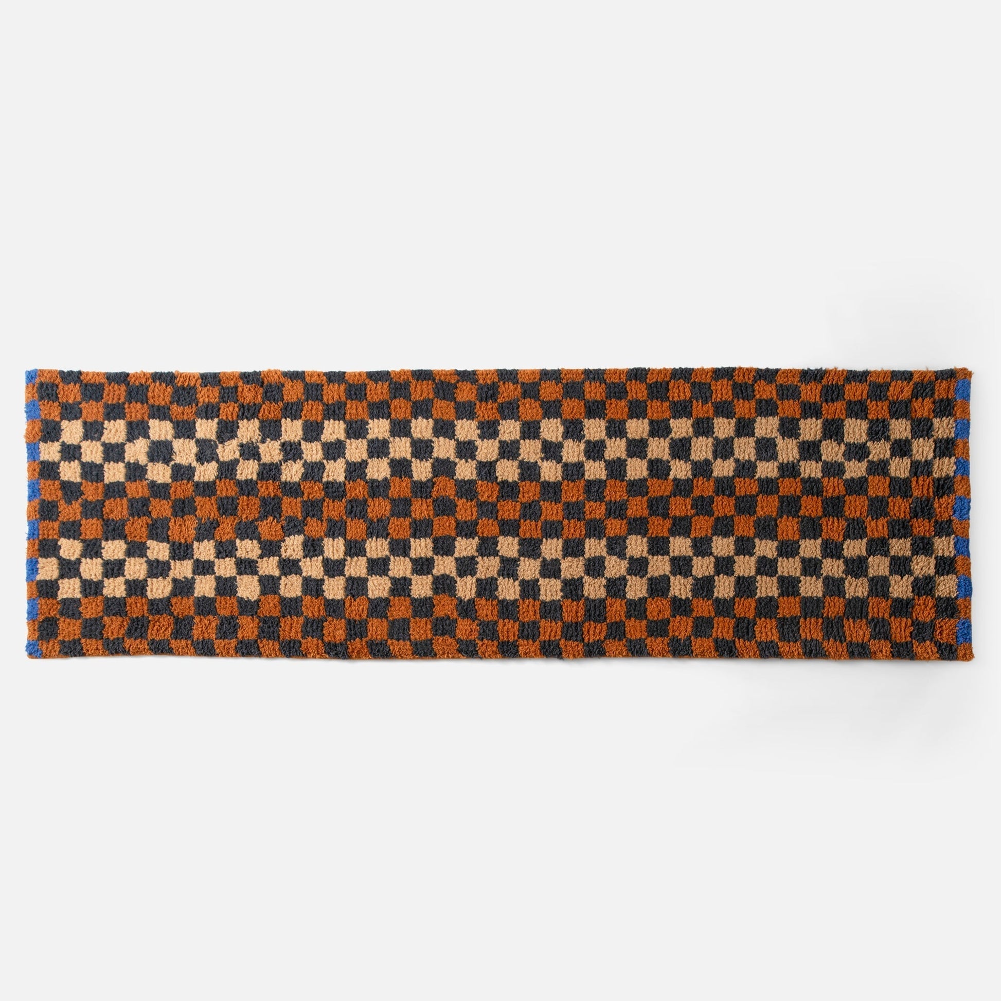 Top edge view of Felix shag wool rug showcasing butterscotch and navy checkerboard pattern and high-pile texture on white background