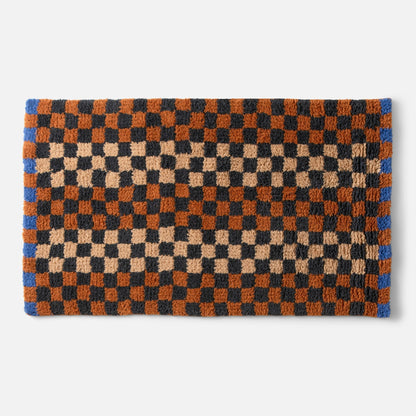 Top edge view of Felix shag rug showing high-pile checkerboard in butterscotch, black and rust with blue border on white background