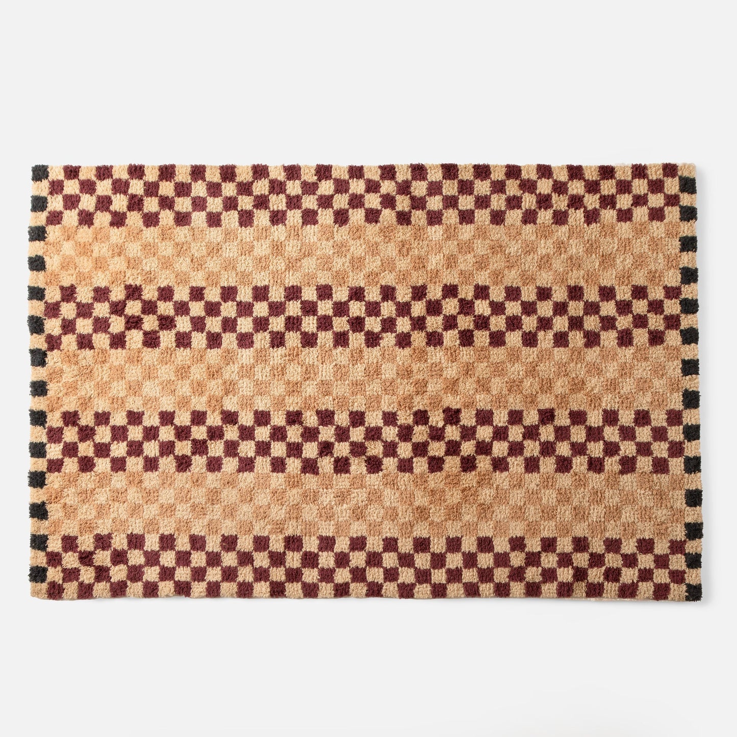 Top edge of Schoolhouse x Clare V. Felix shag wool rug showing butterscotch and burgundy checkered pattern with black border on white background