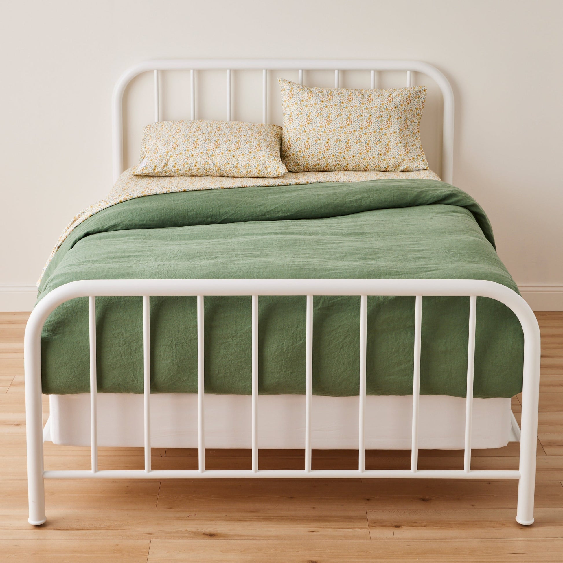 Front of Wallowa Floral percale pillowcase set showcasing chamomile print on bed with green duvet and white frame