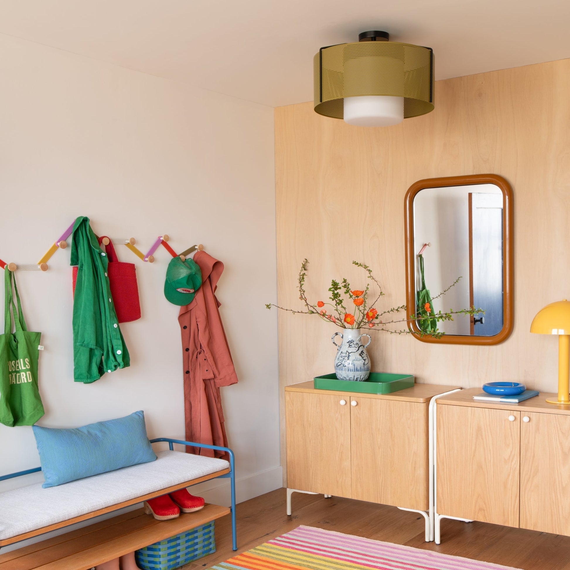 Angled view of Forma Mirror showing rounded rectangular frame and reflection, mounted on a light wood wall in a styled entryway