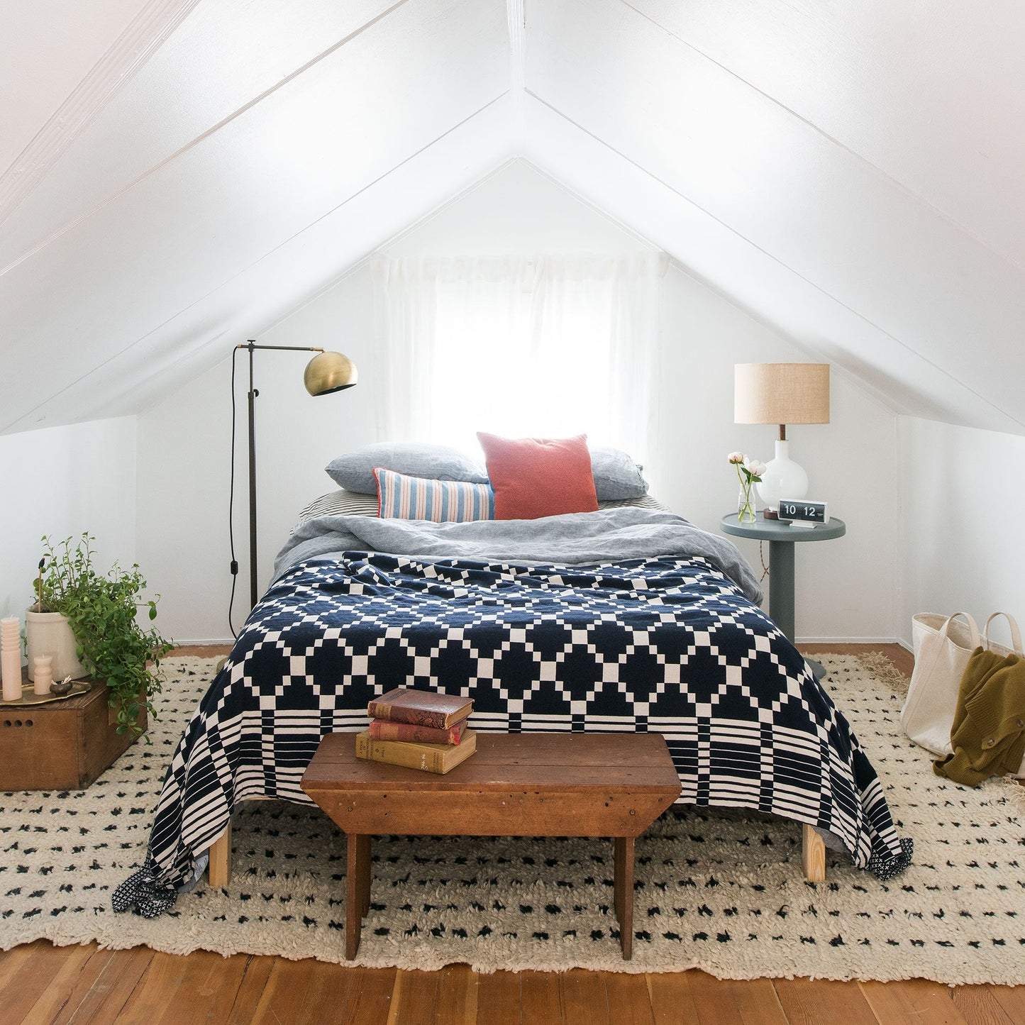 Bed styled with Winter + Summer cotton coverlet (navy geometric) layered with pillows in a bright airy attic bedroom