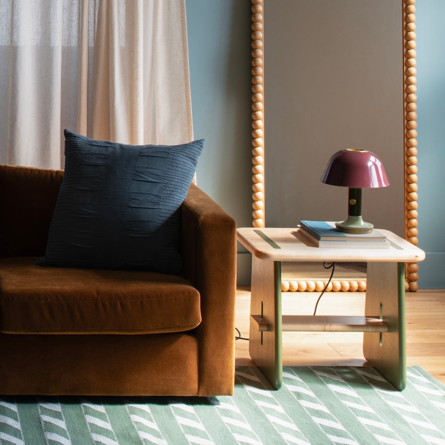 Angled view of Bobbin Mirror showcasing its beaded ash wood frame with a brown sofa, navy pillow, and side table lamp