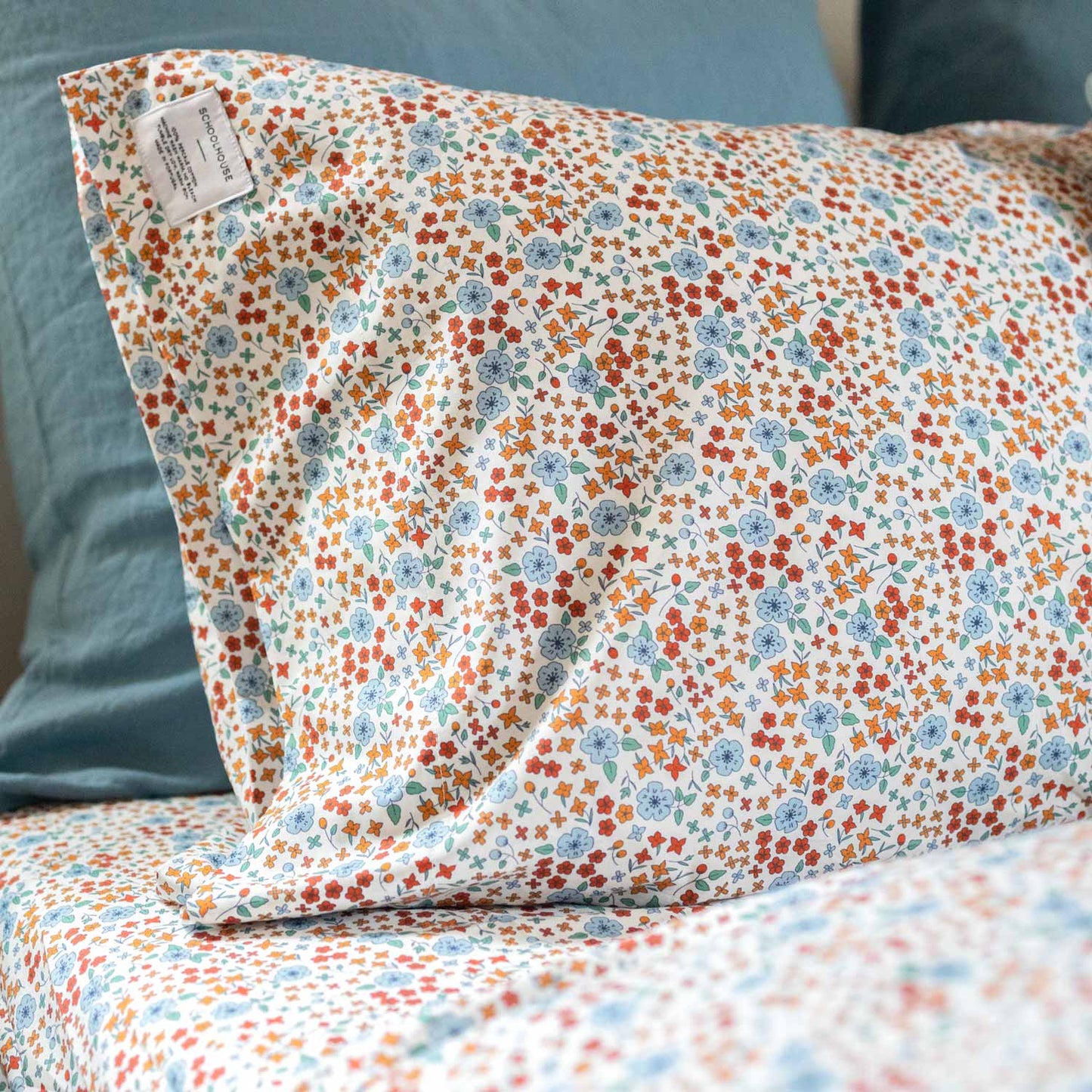 Angled close-up of Wallowa Floral Percale pillowcase showing multicolor floral print on white percale with teal pillow behind