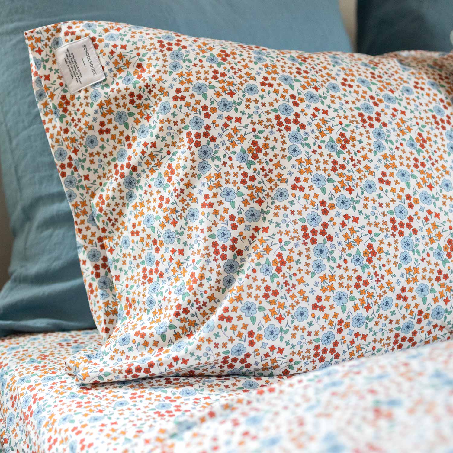 Angled close-up of Wallowa Floral Percale pillowcase showing multicolor floral print on white percale with teal pillow behind