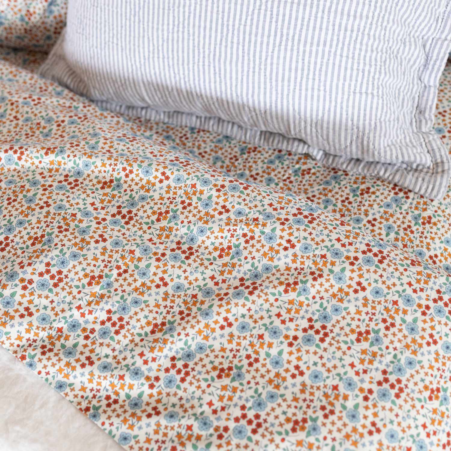 Close-up of Wallowa Floral percale pillowcase set showcasing small blue and orange wildflower print on white with a striped pillow behind