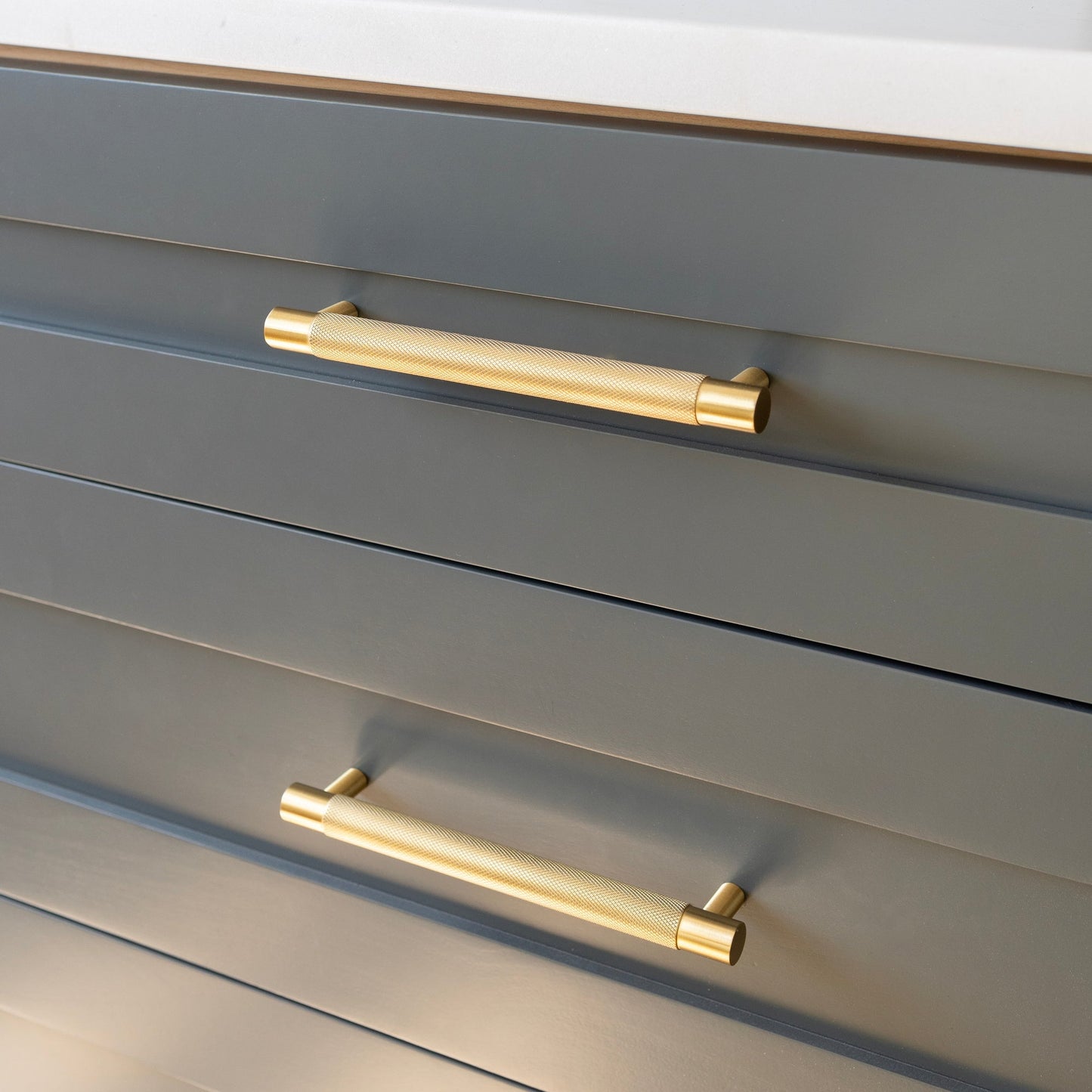 Angled view of the Knurled Pull showcasing its gold textured handle on gray drawers