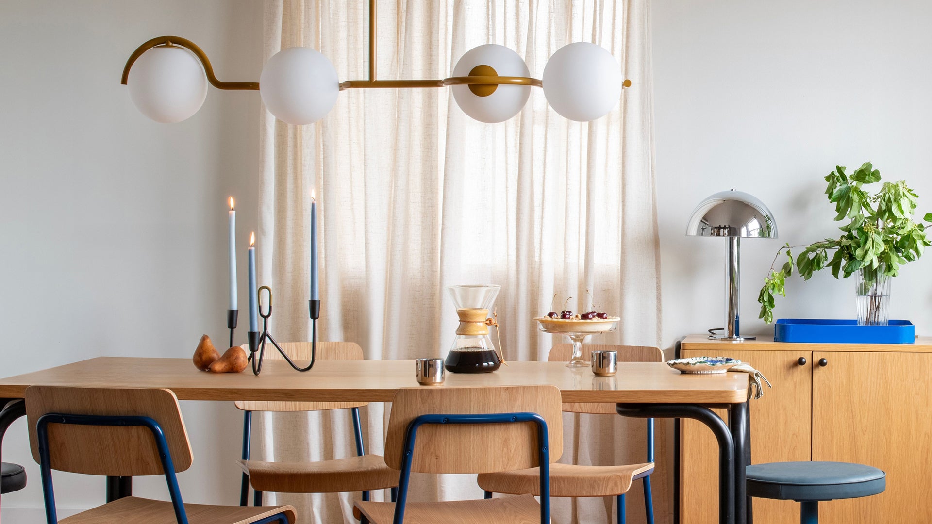 Dining table styled for breakfast with candles, coffee, pie and a brass globe chandelier in a bright neutral dining room